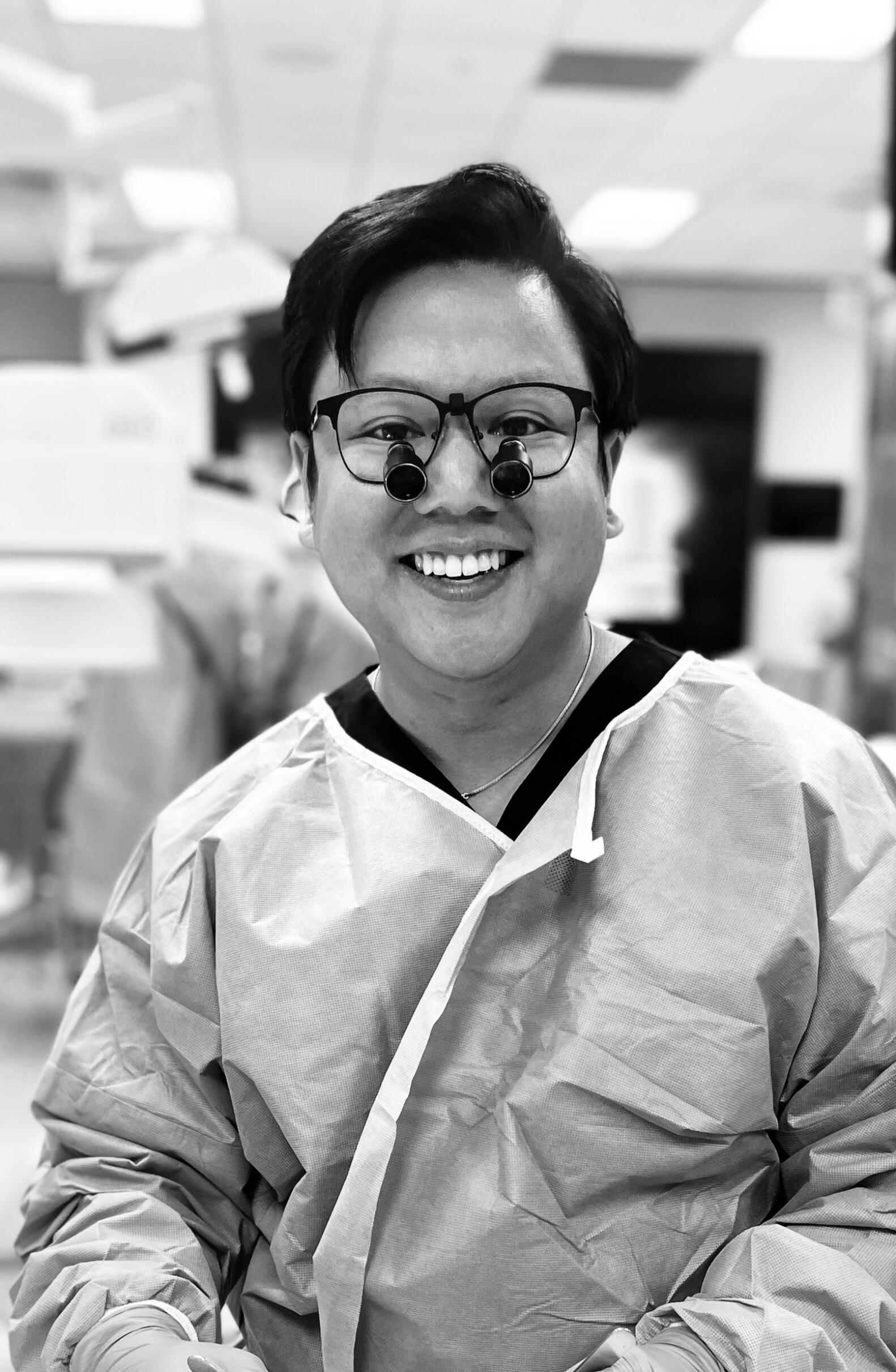Dr. Ersta Ferryanto Surgeon Headshot Dr. Ersta Ferryanto smiling while wearing surgical loupes and gloves during a procedure in a medical setting.